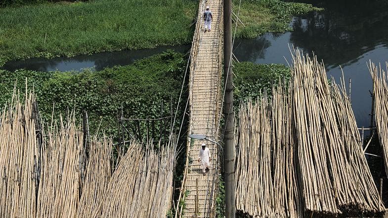 The photo shows two men walk on a bamboo bridge near the bamboo market at Meradia, Banasree, Dhaka on 15 September. Bamboos brought from Gazipur, Tangail, Mymensingh are sold in the market here. Each bamboo sells at Tk 150 to Tk 900 as per their size and length. Photo: Dipu Malakar