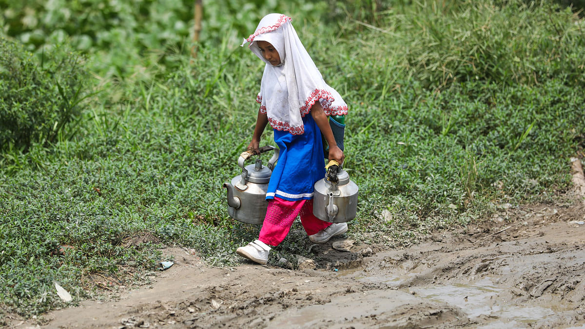 Holding two kettles a little girl in school uniform crosses a road full of puddles and potholes in Canal Par, Pashchim Tengra, Demra on 15 September. Photo: Dipu Malakar
