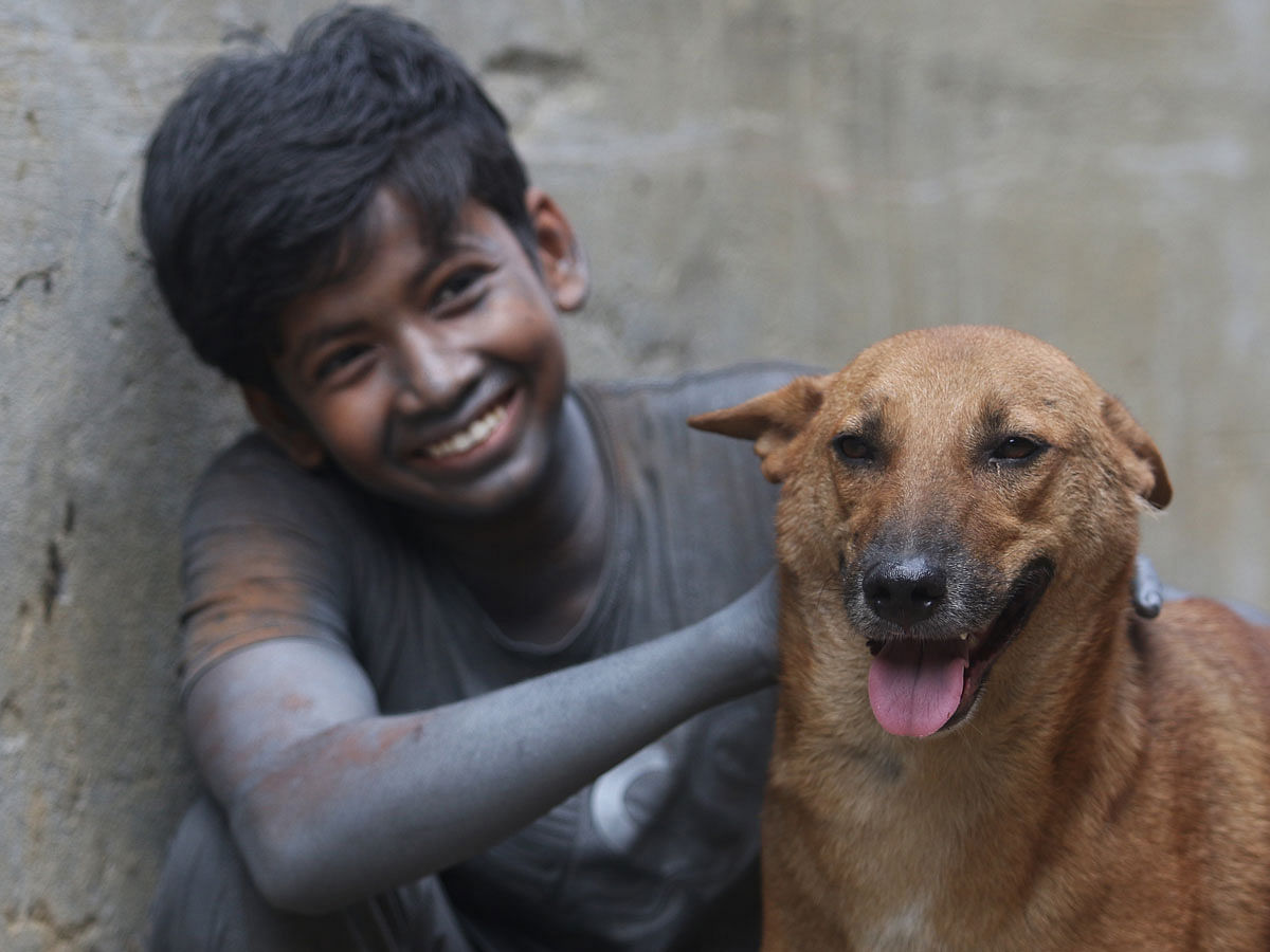 A child worker from a factory at the industrial area of Shyampur, Dhaka plays with a dog. 20 September. Photo: Abdus Salam