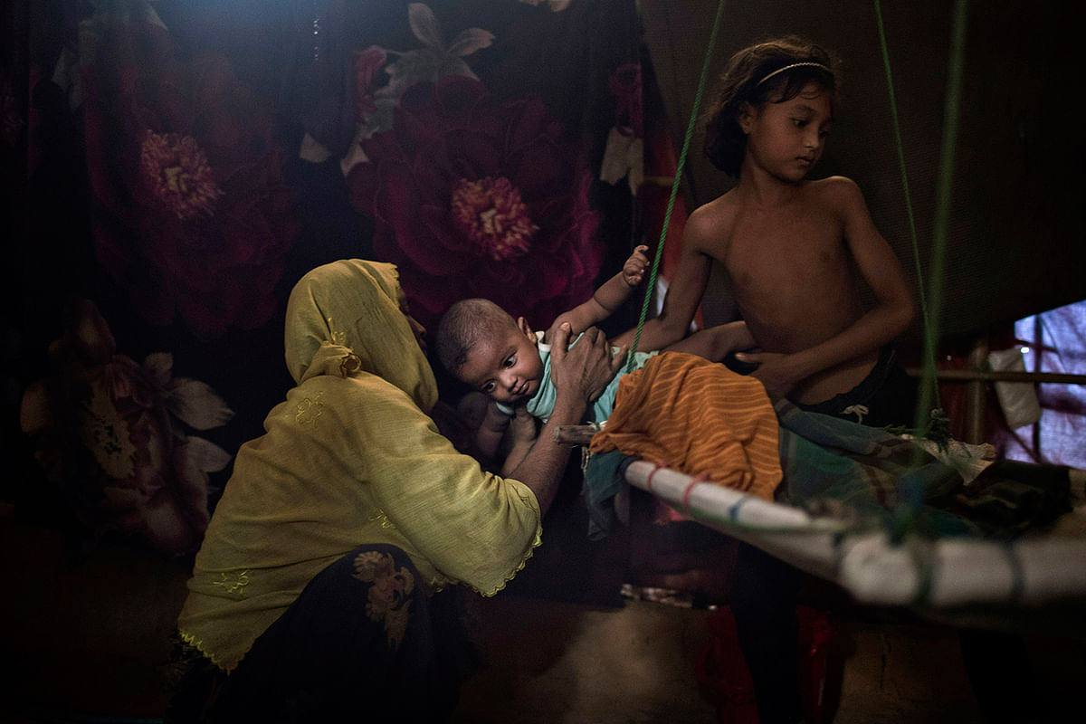 In this 26 June photo, a daughter hands over her baby brother to their mother in their shelter in Kutupalong refugee camp in Bangladesh. Photo: AP