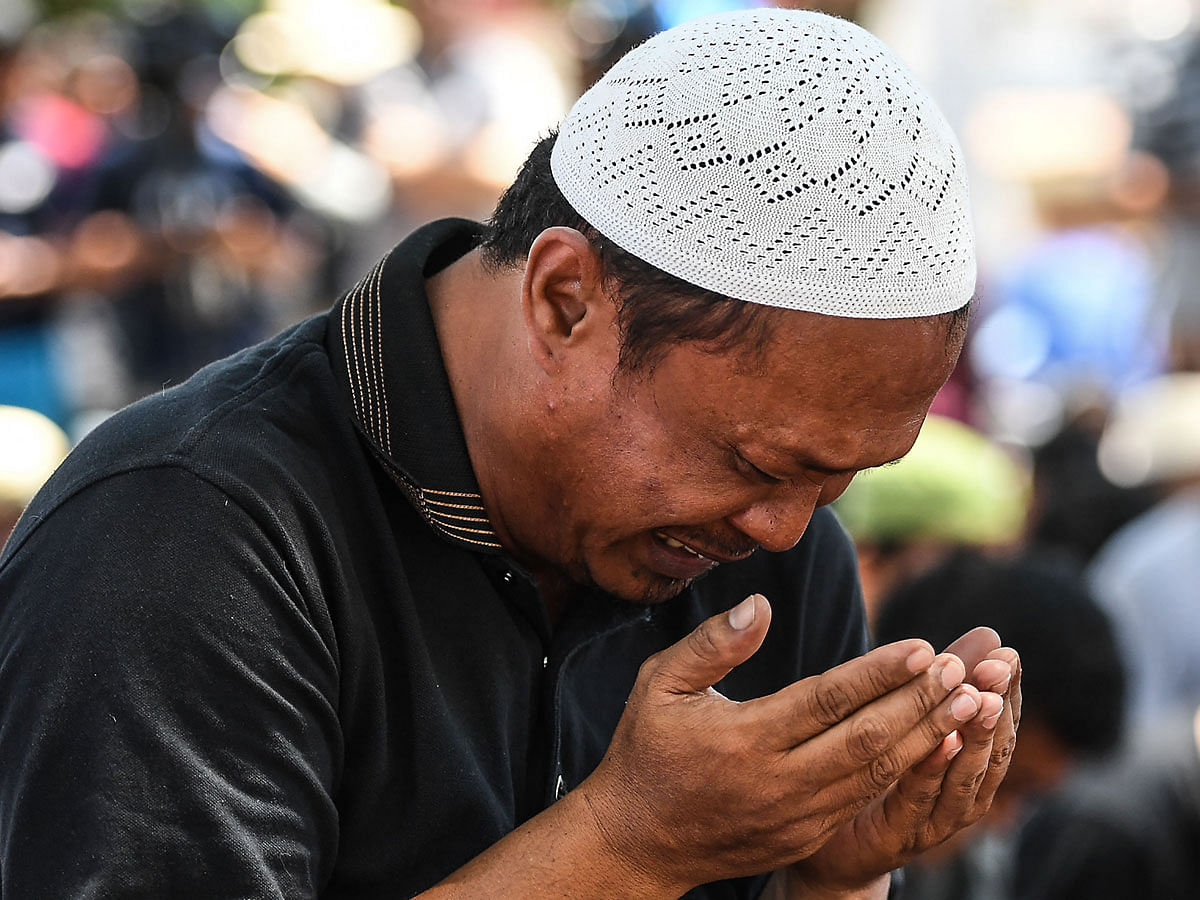 An earthquake and tsunami survivor cries as offers Friday prayers at a makeshift camp set up outside the damaged Agung Darussalam mosque in Palu in Indonesia`s Central Sulawesi on 5 October, following the 28 September earthquake and tsunami. Photo: AFP