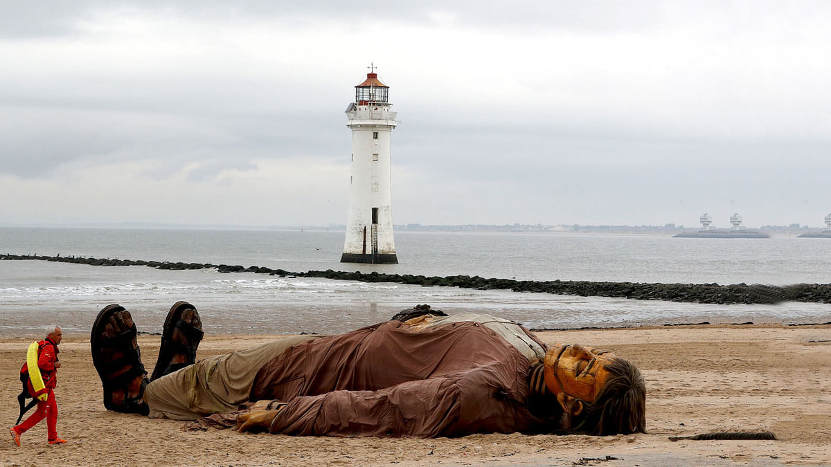 A lifeguard passes one of Royal Deluxe`s giant marionette puppets as it lies on the beach at New Brighton, Britain on 5 October 2018. Photo: Reuters