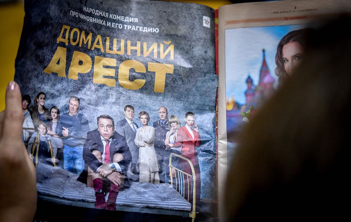 A picture taken on 3 October 2018 in Moscow shows a woman holding a magazine with a promotional ad for the `House Arrest` comedy series. Photo: AFP