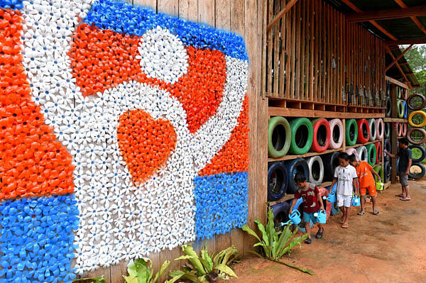 This photo taken on 1 October 2018 shows children watering plants at the Coconut School with a wall decorated by recycled plastic water bottles painted in different colours at Kirirom national park in Kampong Speu province. Photo: AFP