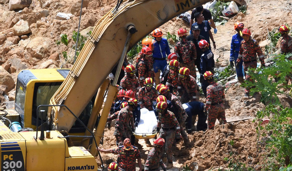 Fire and rescue department personnel retrieve a body from the site of a landslide in Paya Terubong, George Town in in Penang on Saturday. Photo: Bernama