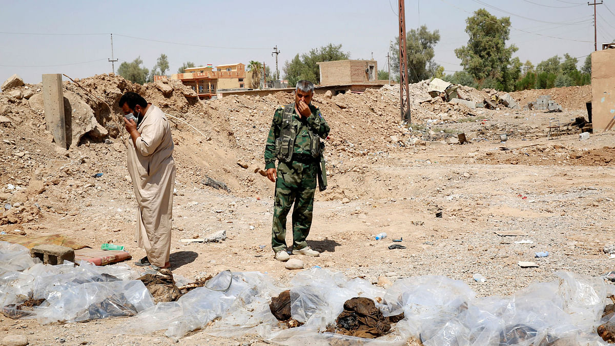 Militia fighters and civilians cover their faces as they stand near bodies recently dug up from a mass grave outside the town of Sulaiman Pek, Iraq on 5 September 2018. Photo: Reuters