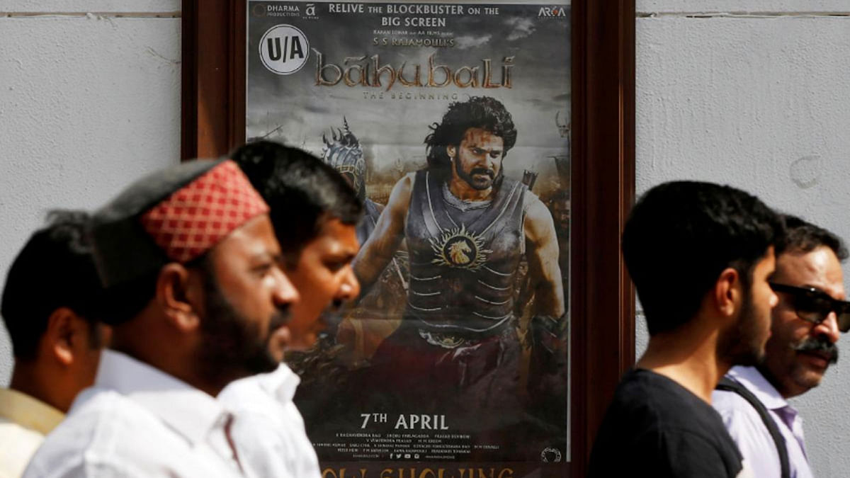 People walk past a poster of an Indian movie `Baahubali: The Beginning` outside a movie theater in New Delhi, on 12 April 2017. -- Photo: Reuters