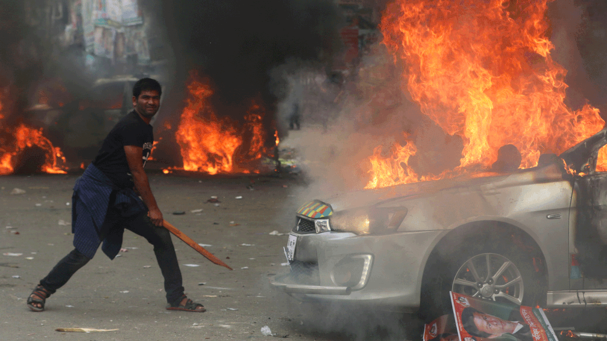 A man stands with a stick in front of a blazing vehicle during clashes between the law enforcement and the members of Bangladesh Nationalist Party at Naya Paltan in Dhaka on 14 November. Photo: Abdus Salam