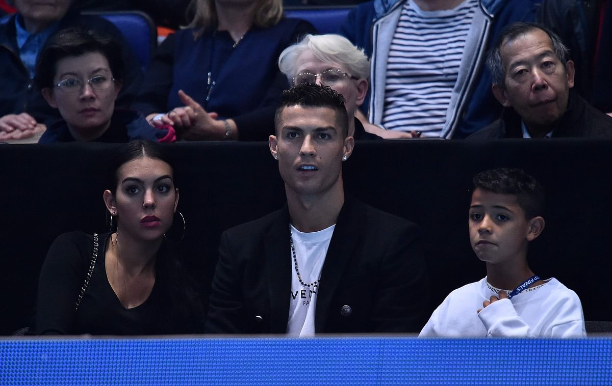 Juventus` Portuguese forward Cristiano Ronaldo (C) sits with Georgina Rodriguez (L) and his son Cristiano Jnr as they watch Serbia`s Novak Djokovic plays against US player John Isner in their men`s singles round-robin match on day two of the ATP World Tour Finals tennis tournament at the O2 Arena in London on 12 November 2018. Photo: AFP