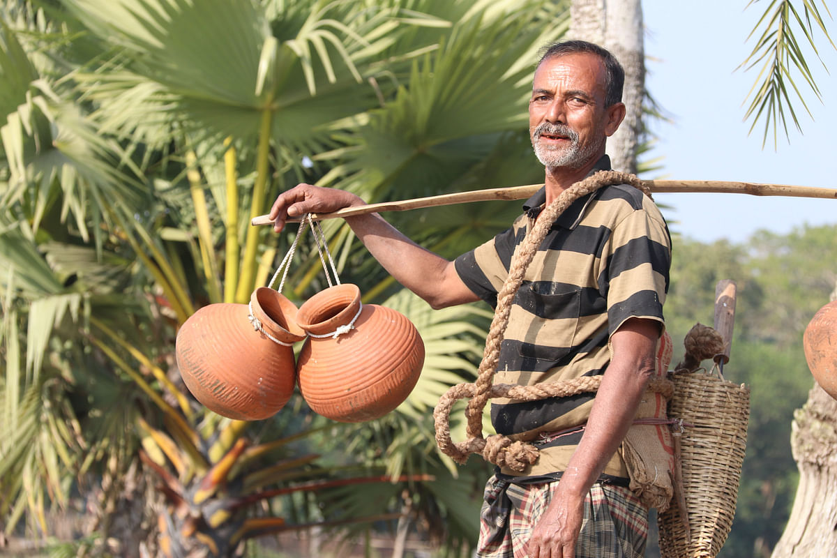 A gachhi (date palm extract collector) smiles with his earthen pots before climbing the tree and placing the pots. Photo: Ehsan-Ud-Doula