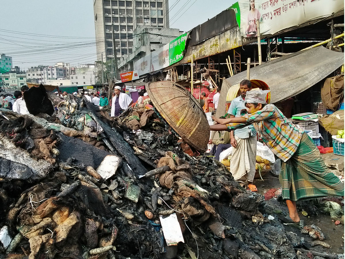 This 21 November photo taken from Karwan Bazar kitchen market in Dhaka shows a labourer working to pile up the damaged items in Dhaka following a fire that broke in the area in morning. Photo: Nusrat Nowrin