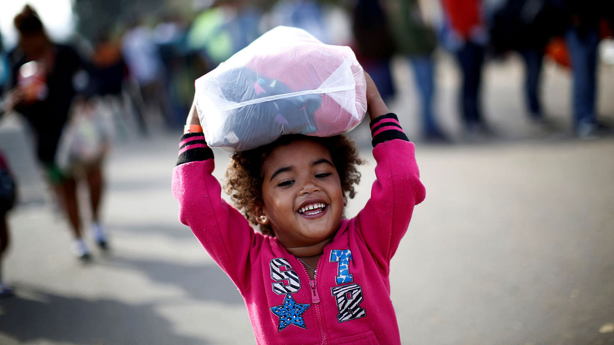 A migrant girl from Honduras, part of a caravan of thousands traveling from Central America en route to the United States, smiles as she carries donated clothes which she and her family received outside a shelter in Tijuana, Mexico on 21 November 2018. Photo: Reuters