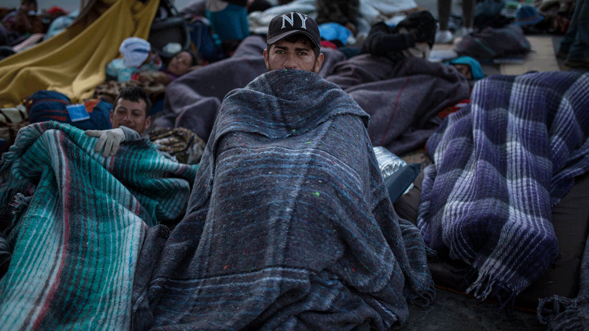 A migrant sits wrapped in a blanket at the Chaparral border crossing in Tijuana, Mexico, Friday early morning, 23 November 2018. The mayor of Tijuana has declared a humanitarian crisis in his border city and says that he has asked the United Nations for aid to deal with the approximately 5,000 Central American migrants who have arrived in the city. Photo: AP