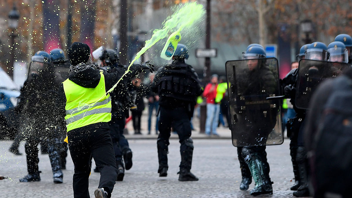 A demonstrator throws a bottle containing yellow painting at riot police officers during a protest of Yellow vests (Gilets jaunes) against rising oil prices and living costs on the Champs Elysees in Paris, on 1 December. Photo: AFP