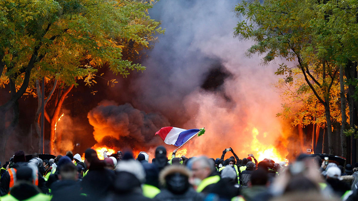 A French flag floats as fire is burning during a protest of Yellow vests (Gilets jaunes) against rising oil prices and living costs, on 1 December 2018 in Paris. Photo: AFP