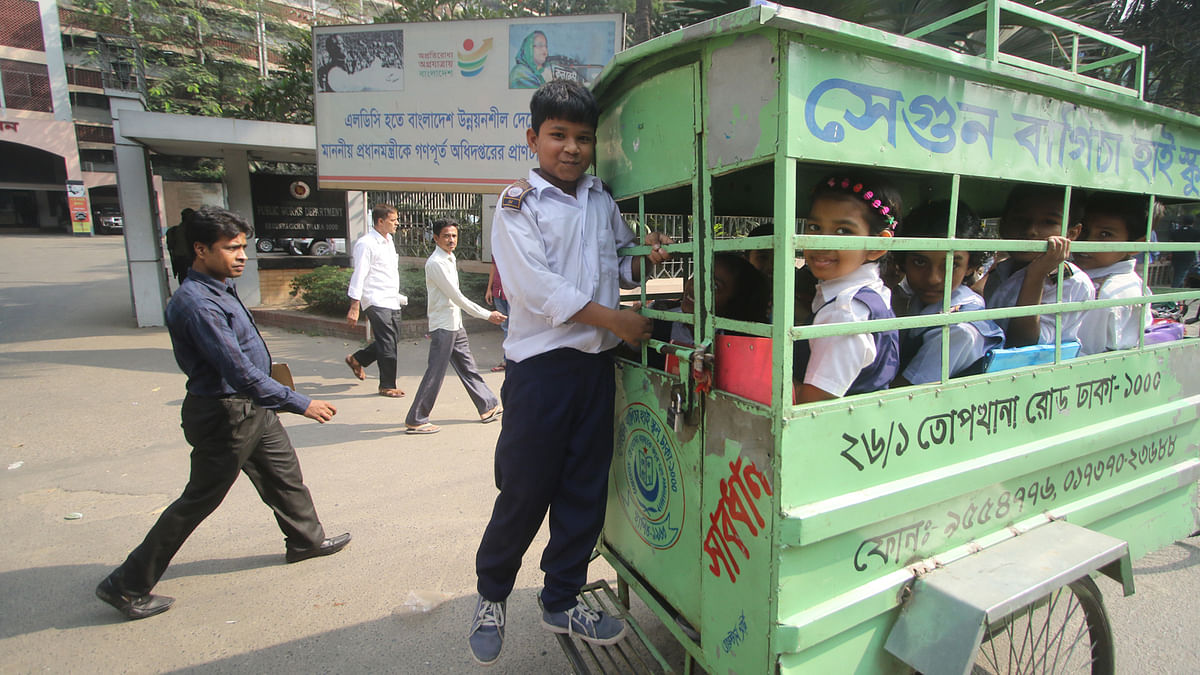 In this photo a boy is seen travelling to his school standing on the pedal of the locked and full school van at Mawlana Bhashani Road near the Supreme Court area in Dhaka on 4 December. Rickshaw vans are forbidden to ply on the thoroughfares leaving the students with no options. Photo: Abdus Salam