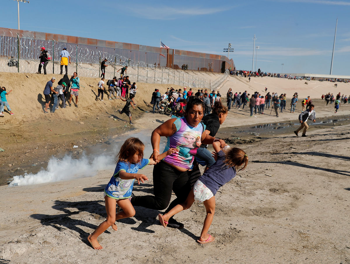 A migrant family, part of a caravan of thousands traveling from Central America to the United States, run away from tear gas in front of the border wall between the US and Mexico in Tijuana, Mexico, 25 November 2018. Photo: Reuters