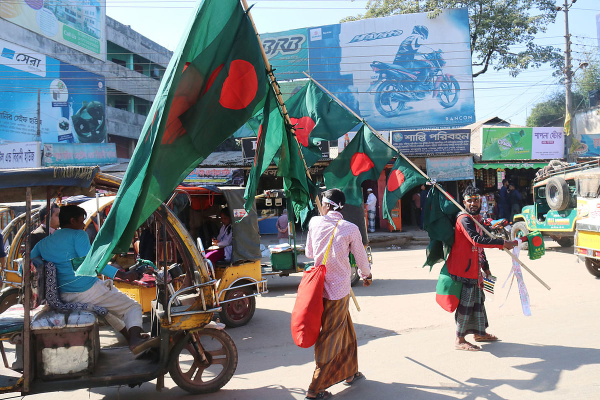 Two men carrying national flags of Bangladesh in the streets. National flags` sale increases in December, the month of victory. The flags are sold at Tk 10 to 250. Shapla chattar, Khagrachhari, 8 December. Photo: Nerob Chowdhury