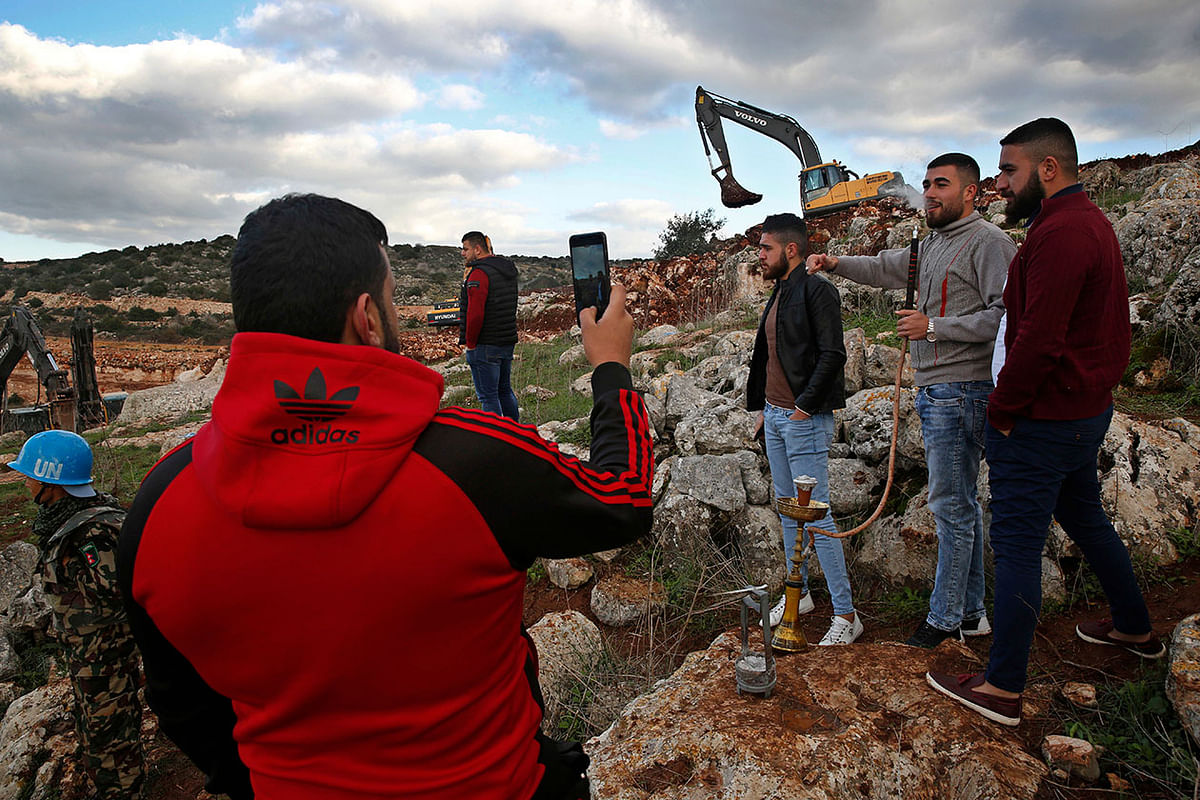 Lebanese villagers smoke a water pipe and take souvenir pictures in front of Israeli excavators, in the southern border village of Mays al-Jabal, Lebanon. Photo: AP
