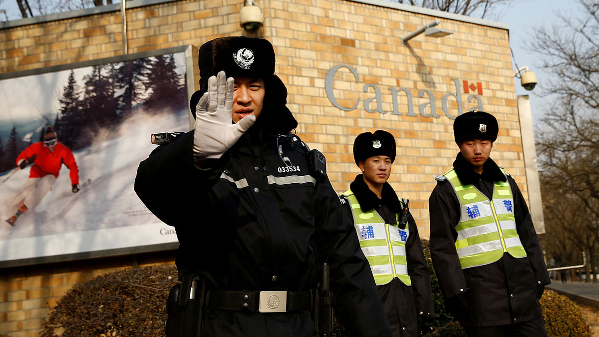 A police officer gestures at the photographer as security staff stand guard outside the Canadian embassy in Beijing, China on 20 December. Photo: Reuters