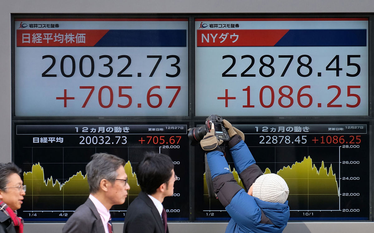 Pedestrians walk past a stock indicator board showing the share price of the Tokyo Stock Exchange (L) and the New York Dow (R) in Tokyo on 27 December 2018 Japanese shares surged nearly four percent on the morning of 27 December, with investors heartened by Wall Street`s best performance in nine years after the White House said Fed Chair Jay Powell would not be fired. Photo: AFP