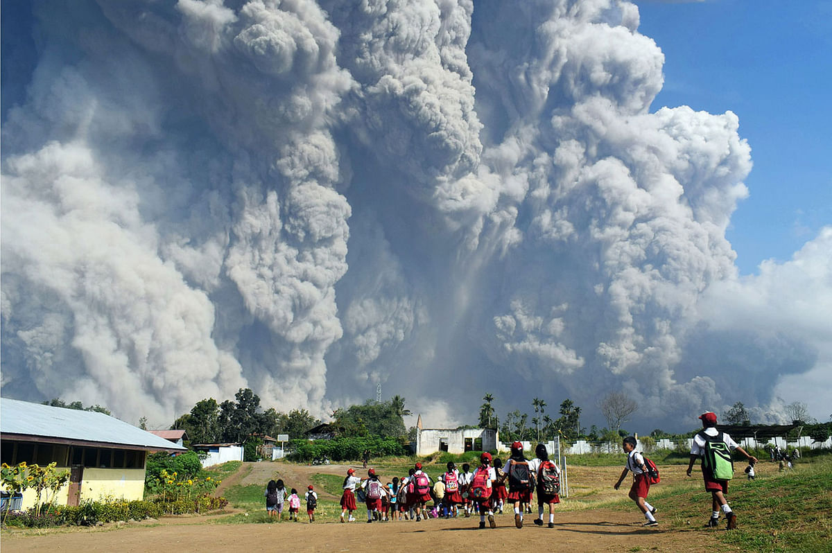 Indonesian schoolchildren walk together at Sipandak elementary school in Tiga Pancur village in Karo, North Sumatra on 19 February 2018, as thick volcanic ash from Mount Sinabung volcano rises into the air following another eruption. Sinabung roared back to life in 2010 for the first time in 400 years and has remained highly active since. Photo: AFP