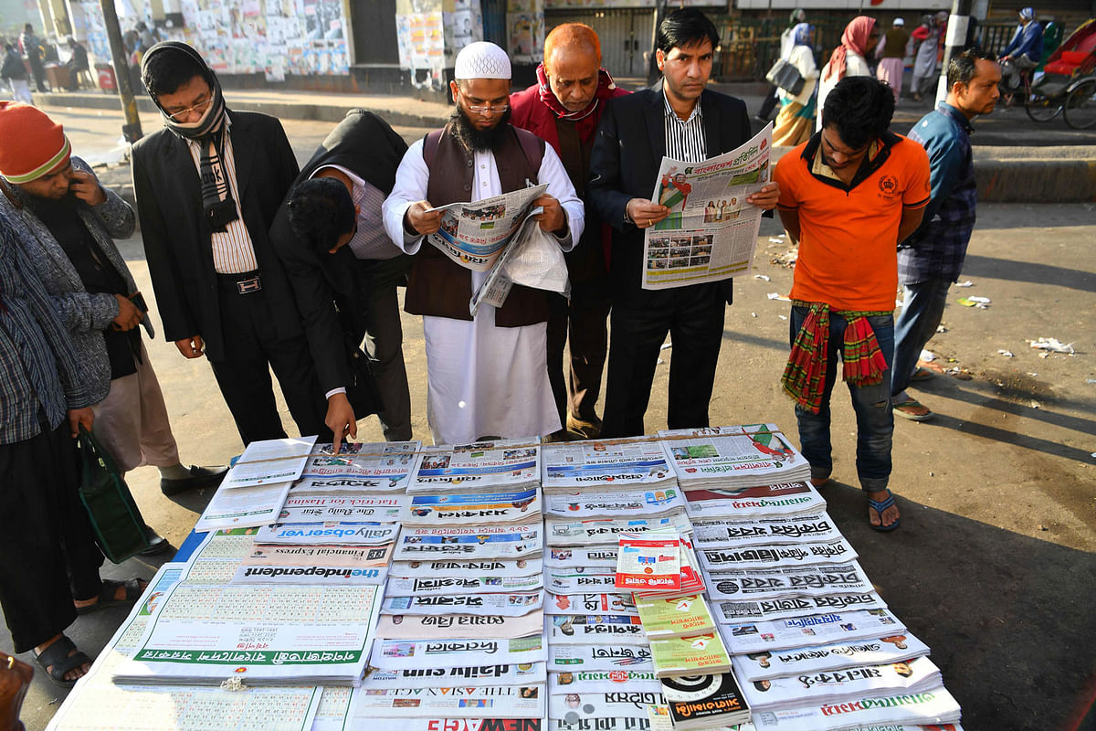 People read newspapers at a newspaper stand in Dhaka on 31 December. Photo: AFP