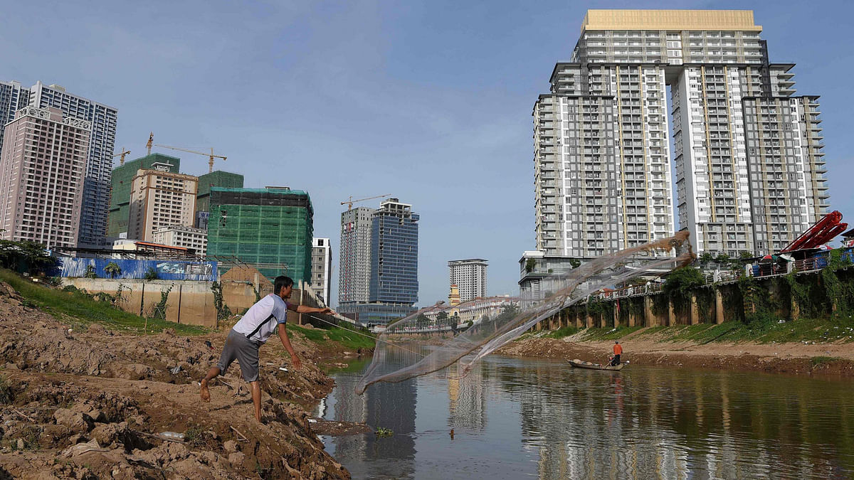 This photograph taken on 12 December 2018 shows a Cambodian man fishing in a canal in front of under-construction high-rise buildings in Phnom Penh. Photo: AFP