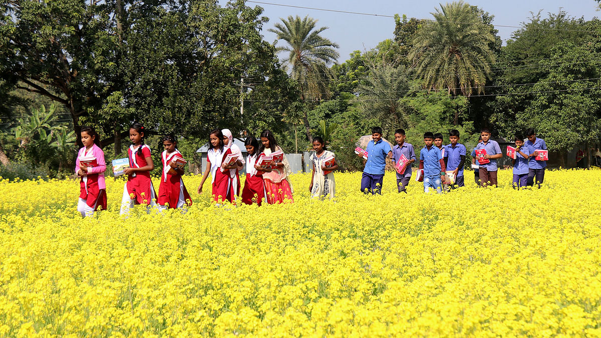 Students return home crossing mustard fields as they hold new textbooks received during the textbook festival held across the country on 1 January. Photo: Hassan Mahmud