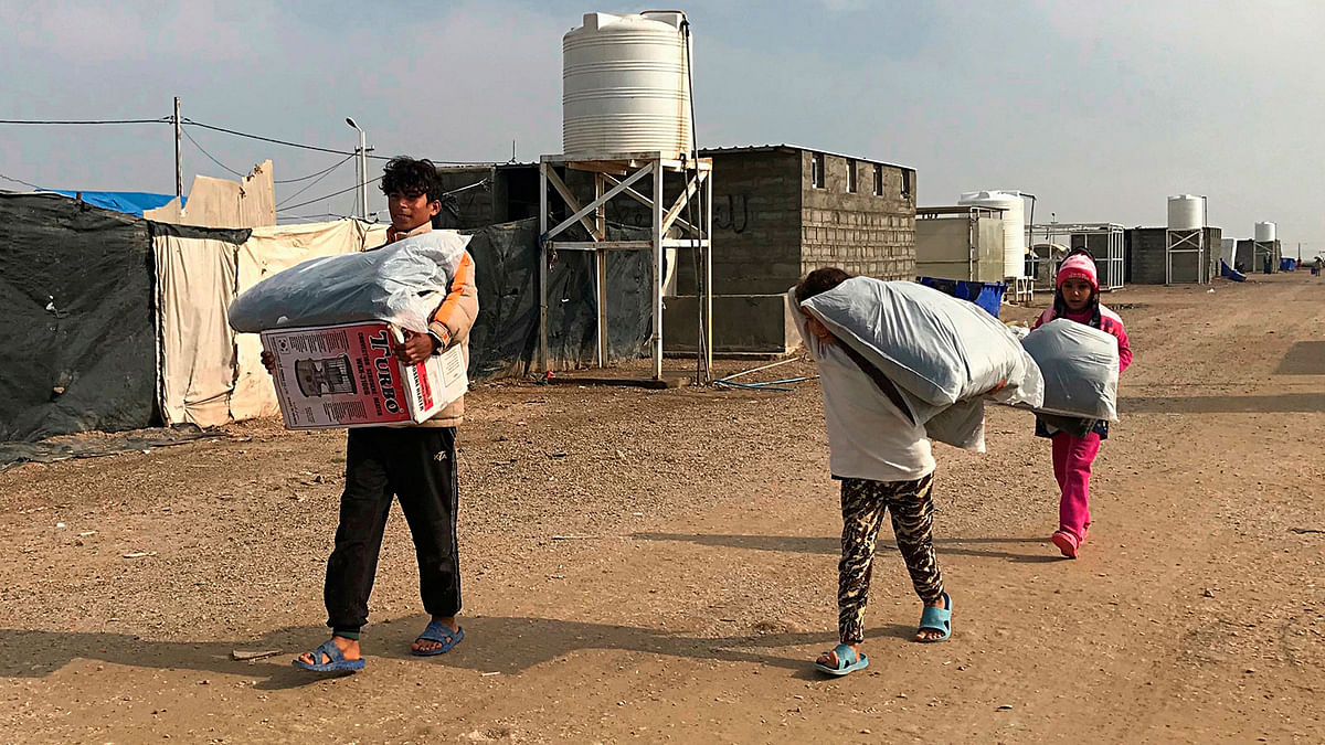 In this Dec. 26, 2018 photo, displaced people carry humanitarian aid at the Amariyat al-Fallujah camp, in Anbar province, Iraq. A little over a year since the country fought its last battle against IS, but well before it has gotten a handle on reconstruction, Iraq is closing its camps for the displaced and casting vulnerable families into a maelstrom of peril. Photo: AP