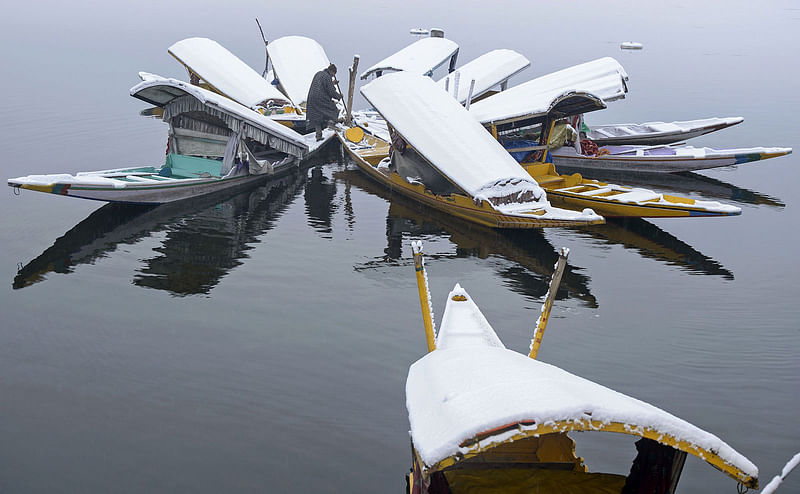 A Kashmiri boatman clears snow from shikara boats in Dal Lake after fresh snowfall in Srinagar on 11 January 2019. Photo: AFP