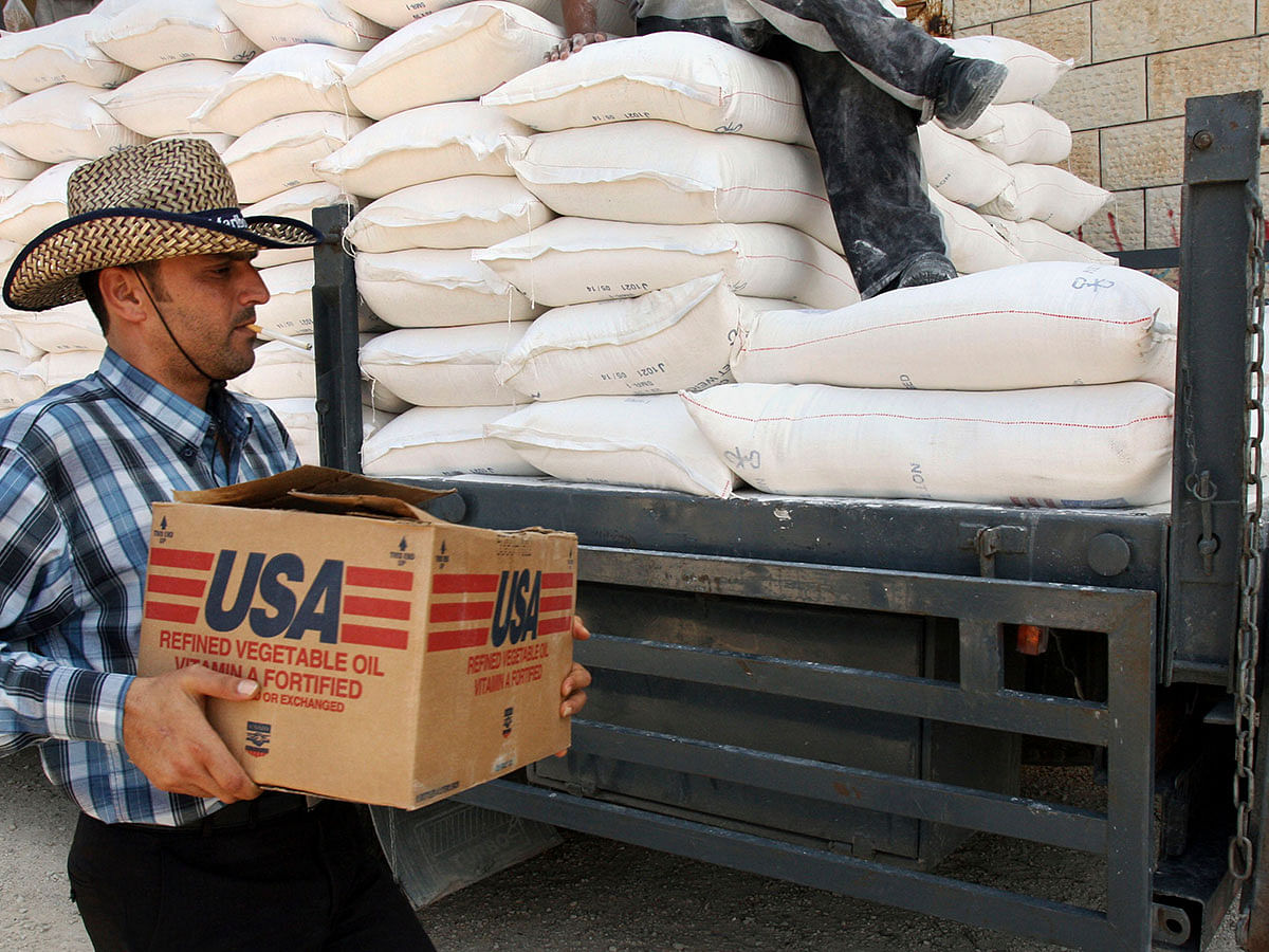 In this 4 June 2008 file photo, a Palestinian carries a box of vegetable oil as he walks past bags of flour, both donated by the United States Agency for International Development, at a depot in the West Bank village of Anin near Jenin. Photo: AP