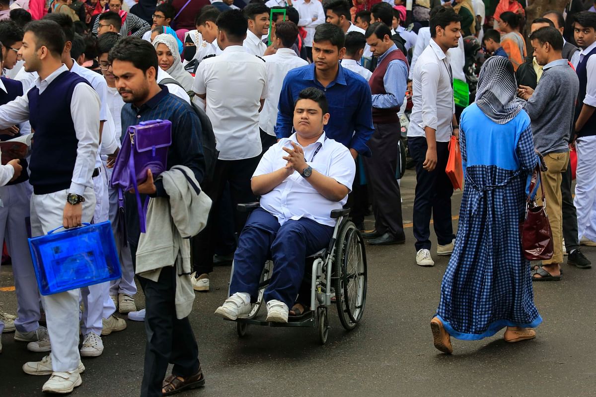 A man pushing a wheelchair with a physically challenged examinee amid the students entering exam halls during the SSC and equivalents exams starting across the country on Saturday. Motijheel Ideal School and college, Dhaka on 2 February. Photo: Hasan Raja