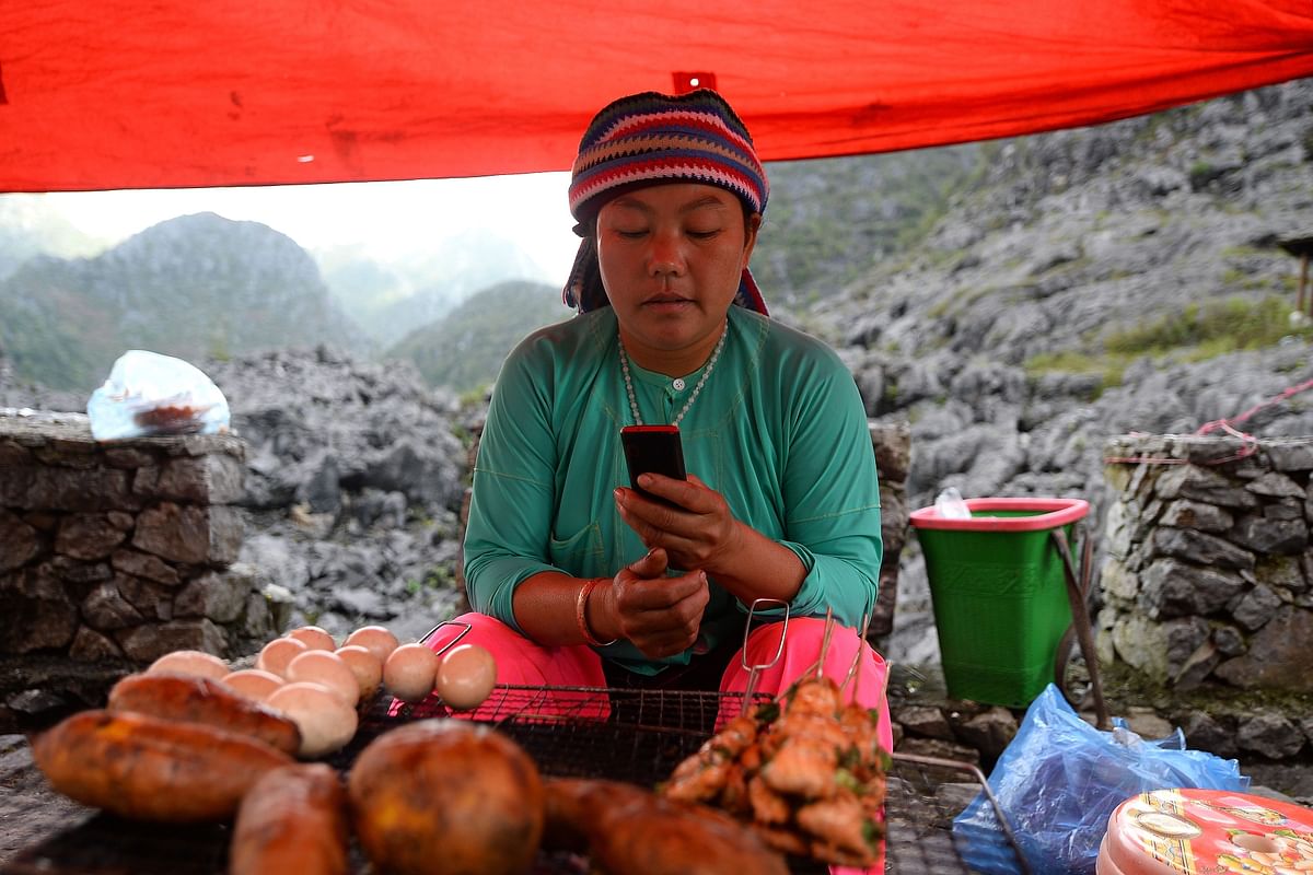 This picture taken on 26 October 2018 shows ethnic Hmong food vendor Va Thi May checking her phone while waiting for customers at her stall in Dong Van district, northern Vietnam`s Ha Giang province. Photo: AFP