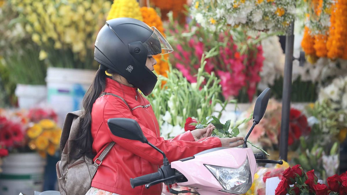 Being seated on a motorcycle a woman buys flower at the flower market in Shahbagh, Dhaka on 14 February. Photo: Abdus Salam