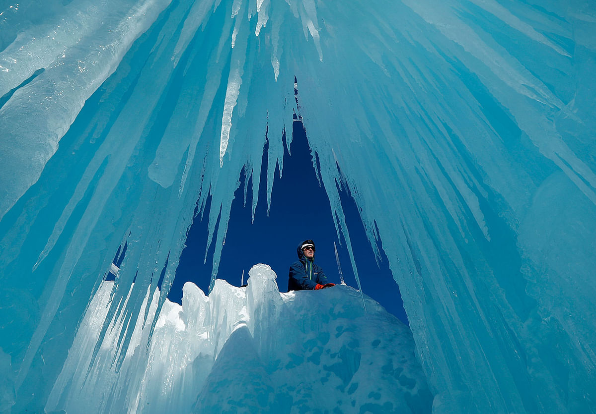 In this 26 January 2019 photo, Matt Pasciuto places an icicle at the top of a wall at Ice Castles in North Woodstock, NH. Slushy snow is used as quick-freezing mortar to hold icicles in place. The spray from sprinklers will help grow the icicles into walls and caverns. Photo: AP