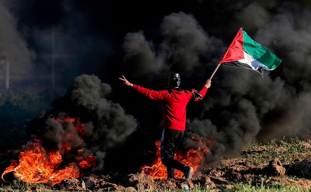 A Palestinian protester waves the national flag next to burning tires during clashes with Israeli forces following a demonstration near the fence along the border with Israel, east of Gaza City, on 8 March, 2019. Photo: AFP