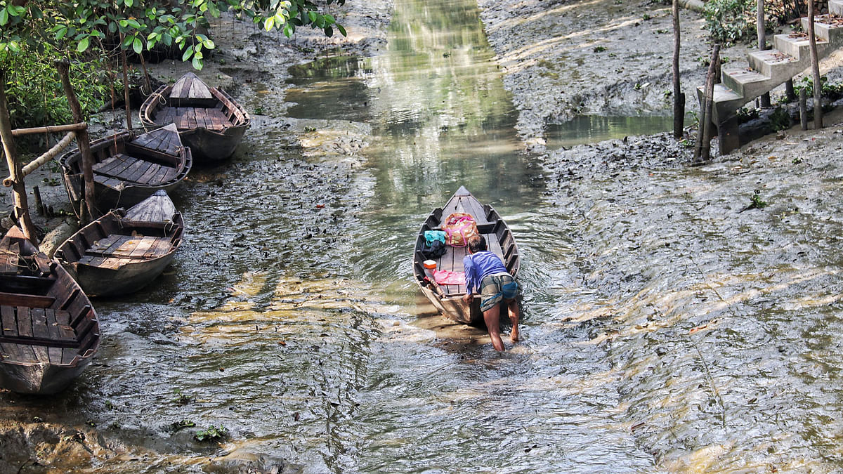 A man pushes his boat in the mud as the ebb causes the canal water to recede at Sohaghdal, Nechharabad in Pirojpur on 9 March. Photo: Saddam Hossain