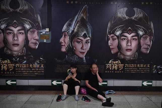 A man and woman rest in front of posters for the movie Asura at a subway station in Beijing on 17 July 2018. AFP File Photo