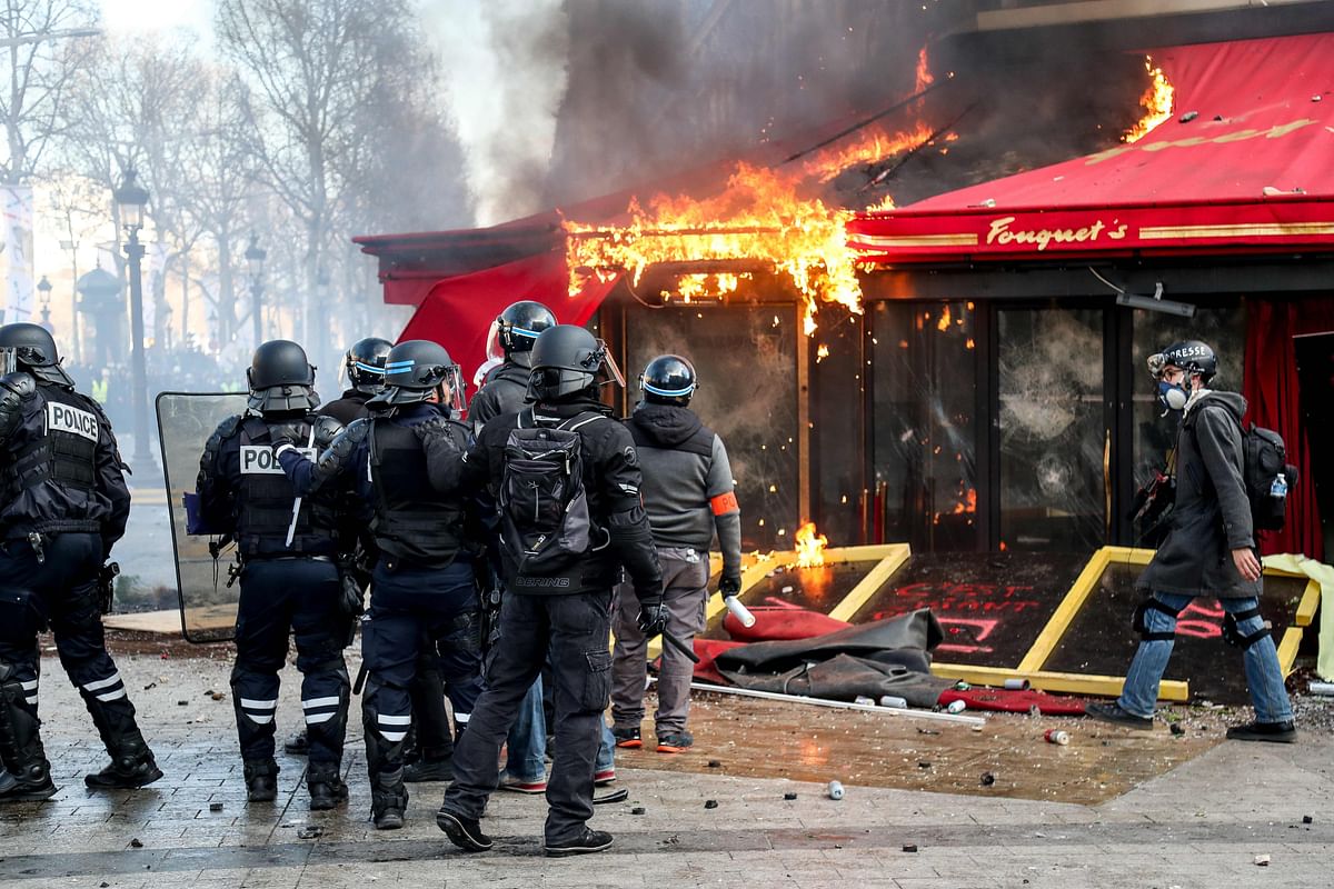 In this file photo taken on 16 March Riot police forces stand next to the restaurant `Le Fouquet`s` burning during clashes between riot police forces and Yellow Vest protesters on the Champs-Elysees in Paris on the 18th consecutive Saturday of demonstrations called by the `Yellow Vest` (gilets jaunes) movement. AFP File Photo
