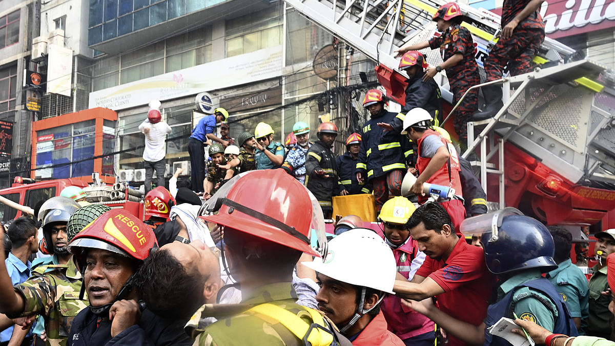 Firefighters carry a casualty next to a burning office building in Dhaka on 28 March 2019. Photo: AFP