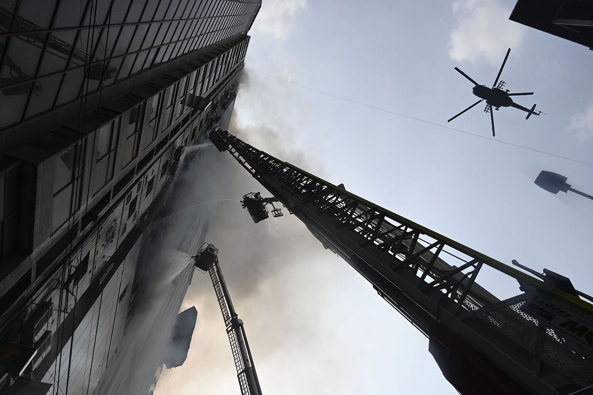 A helicopter carries water to drop on a burning office building as Bangladeshi firefighters on ladders work to extinguish the blaze in Dhaka on 28 March 2019. Photo: AFP