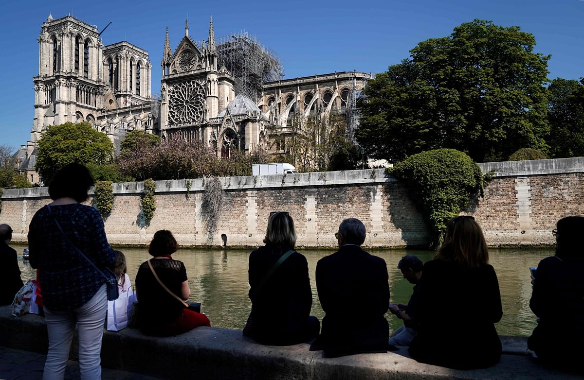 People sit on the bank of the Seine river in front of Notre-Dame de Paris Cathedral in Paris on 19 April, 2019, four days after a fire devastated the cathedral. Photo: AFP
