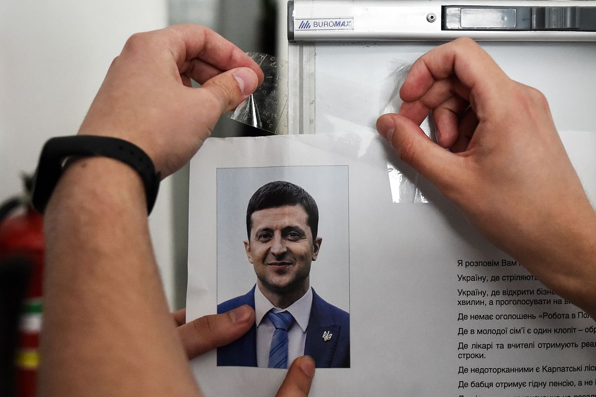 A member of a local electoral commission hangs an information placard bearing a portait of Ukrainian comedian and presidential candidate Volodymyr Zelensky as he prepares a polling station for the upcoming presidential election in Kiev, on 20 April 2019 on the eve of the second round of the Presidential election in Ukraine. Photo: AFP