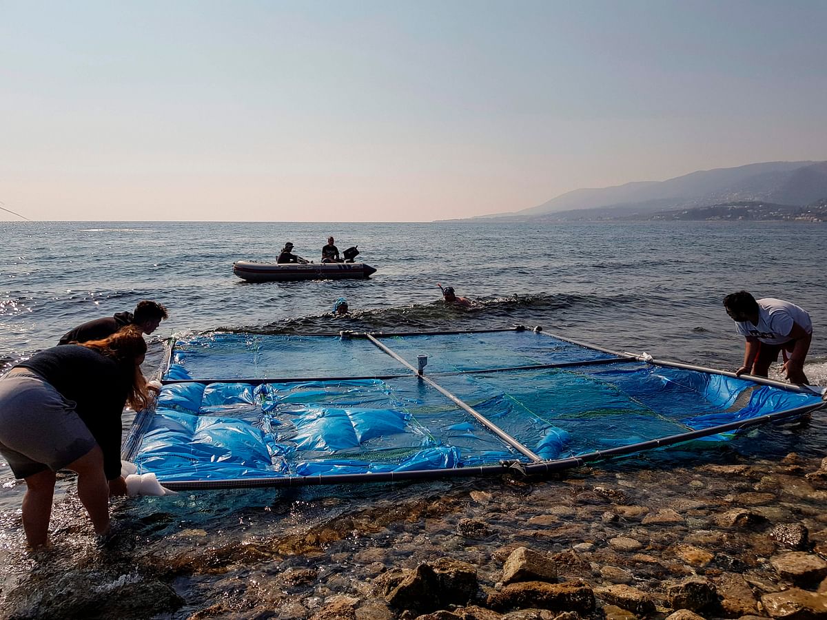 Greek university students gently deposits a wall-sized PVC frame on the surface before divers moor them at sea at a beach in the island of Lesbos on 18 April, 2019. Photo: AFP