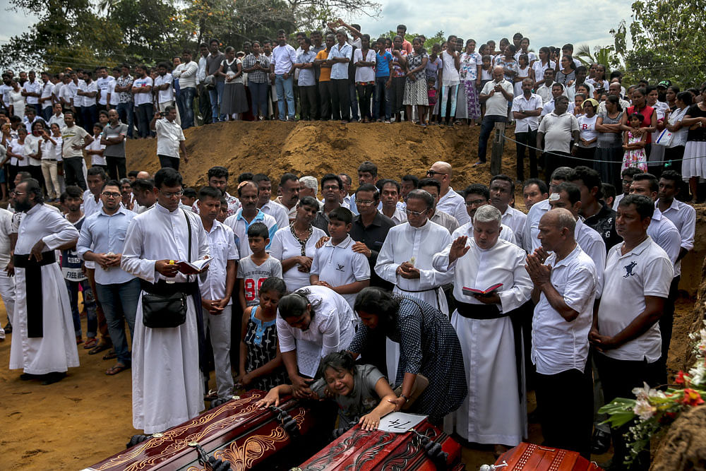A woman reacts next to two coffins during a mass burial of victims, two days after a string of suicide bomb attacks on churches and luxury hotels across the island on Easter Sunday, at a cemetery near St. Sebastian Church in Negombo, Sri Lanka on 23 April 2019. Photo: Reuters