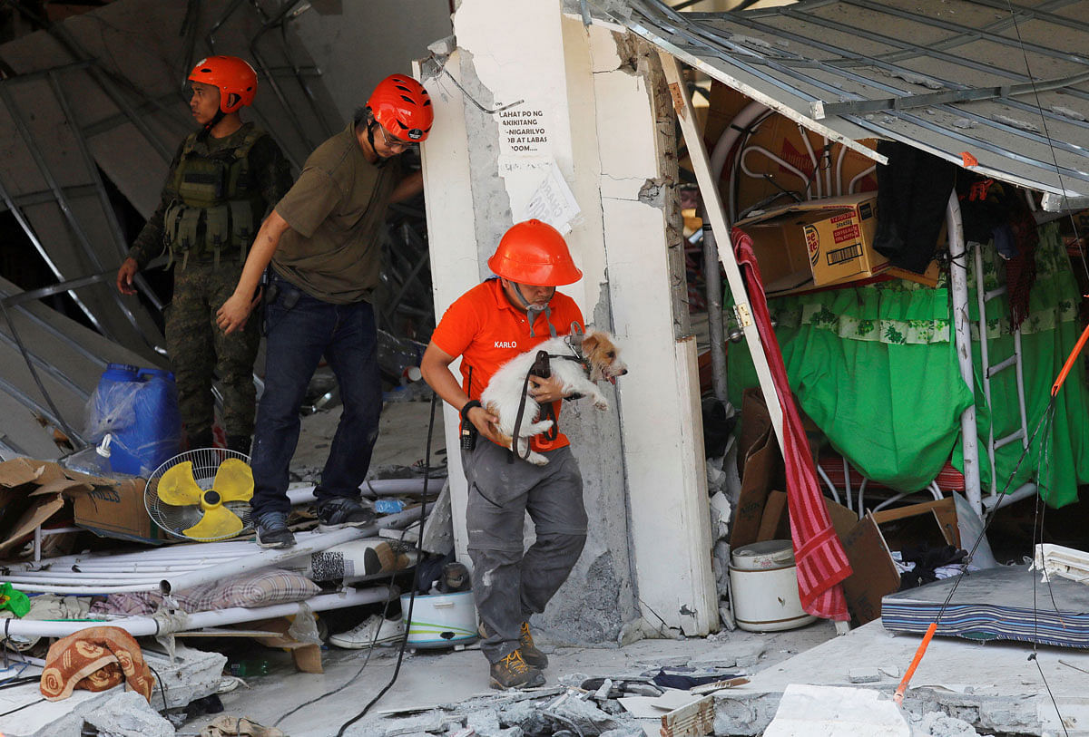 A rescuer carries a search dog as they try to reach survivors at a collapsed four-storey building following an earthquake in Porac town, Pampanga province, Philippines, on 23 April 2019. Photo: Reuters