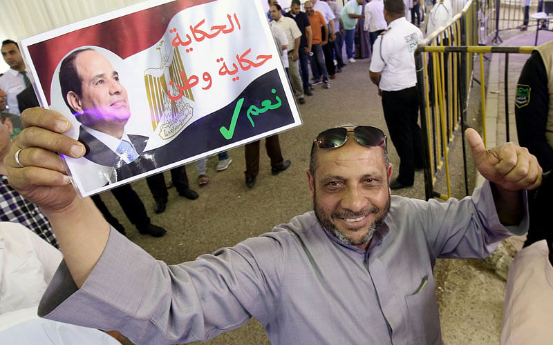 An Egyptian man, living in Kuwait, gives the thumbs up as he waves a placard bearing the portrait of president Abdel Fattah al-Sisi before casting their votes in a referendum on constitutional amendments, at the Egyptian embassy in Kuwait City on 19 April 2019. Photo: AFP