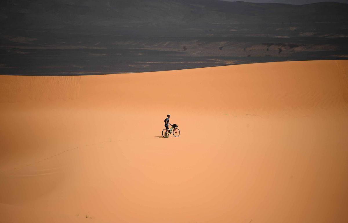 A competitor pushes a bicycle along a sand dune during Stage 2 of the 14th edition of Titan Desert 2019 mountain biking race between Merzouga and Ouzina on 29 April 2019. Photo: AFP