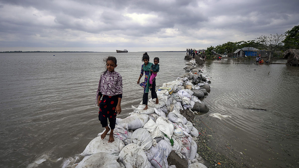 Bangladeshi children walk over the top of a sandbag embankment that was breached by high waters in Khulna on 4 May, 2019, as cyclone Fani reached Bangladesh. Photo: AFP